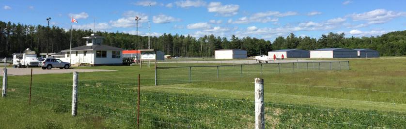 The Township of Algonquin Highlands Stanhope Municipal Airport - photo of the terminal building and airport grounds, with aircraft hangers in the background