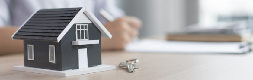 Photo of a small model of a house on a desk with paperwork in background