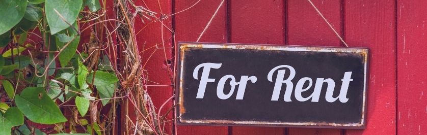 Photo of green vines against a red wall with sign posted saying "For Rent"